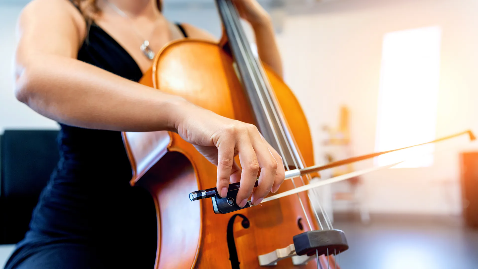Eine Frau streicht mit einem Bogen über die Saiten des Violoncellos.