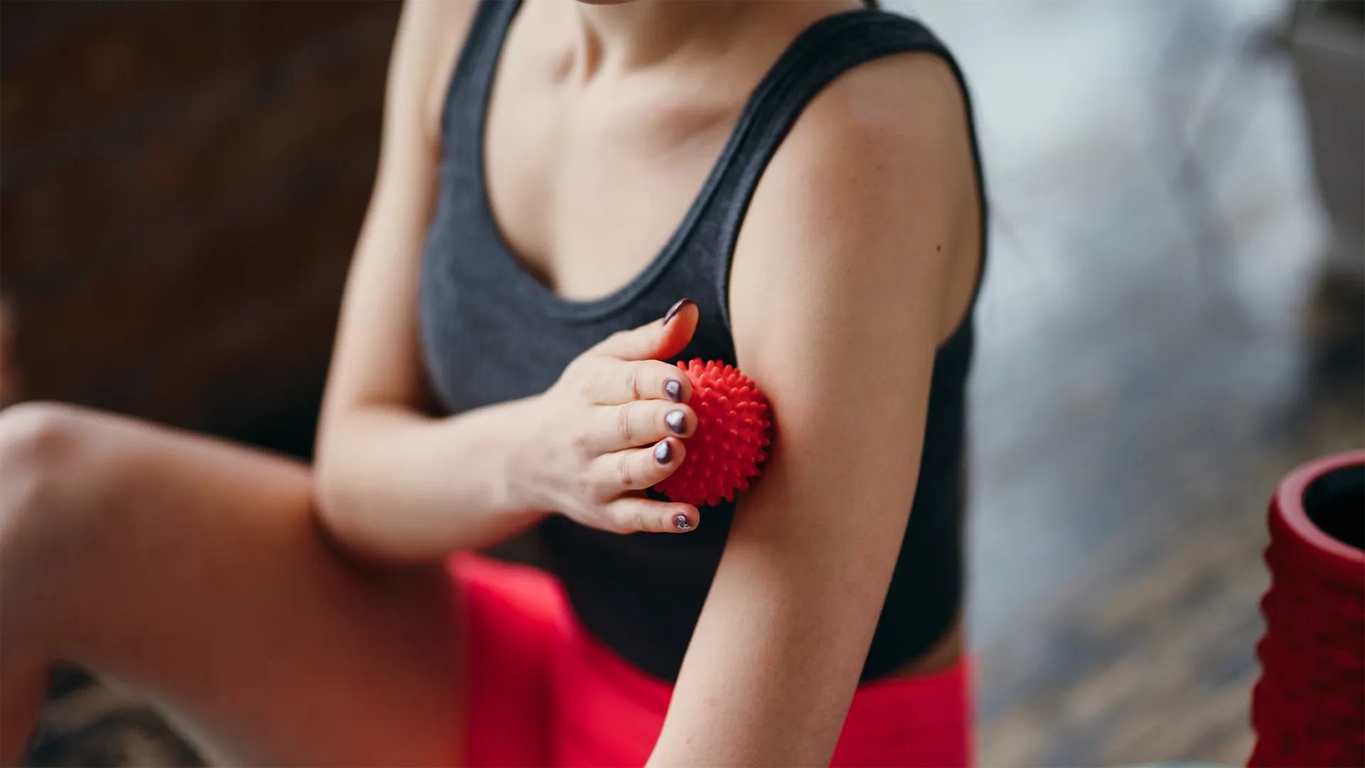 Person massiert die Faszien am Oberarm mit einem roten Noppenball.