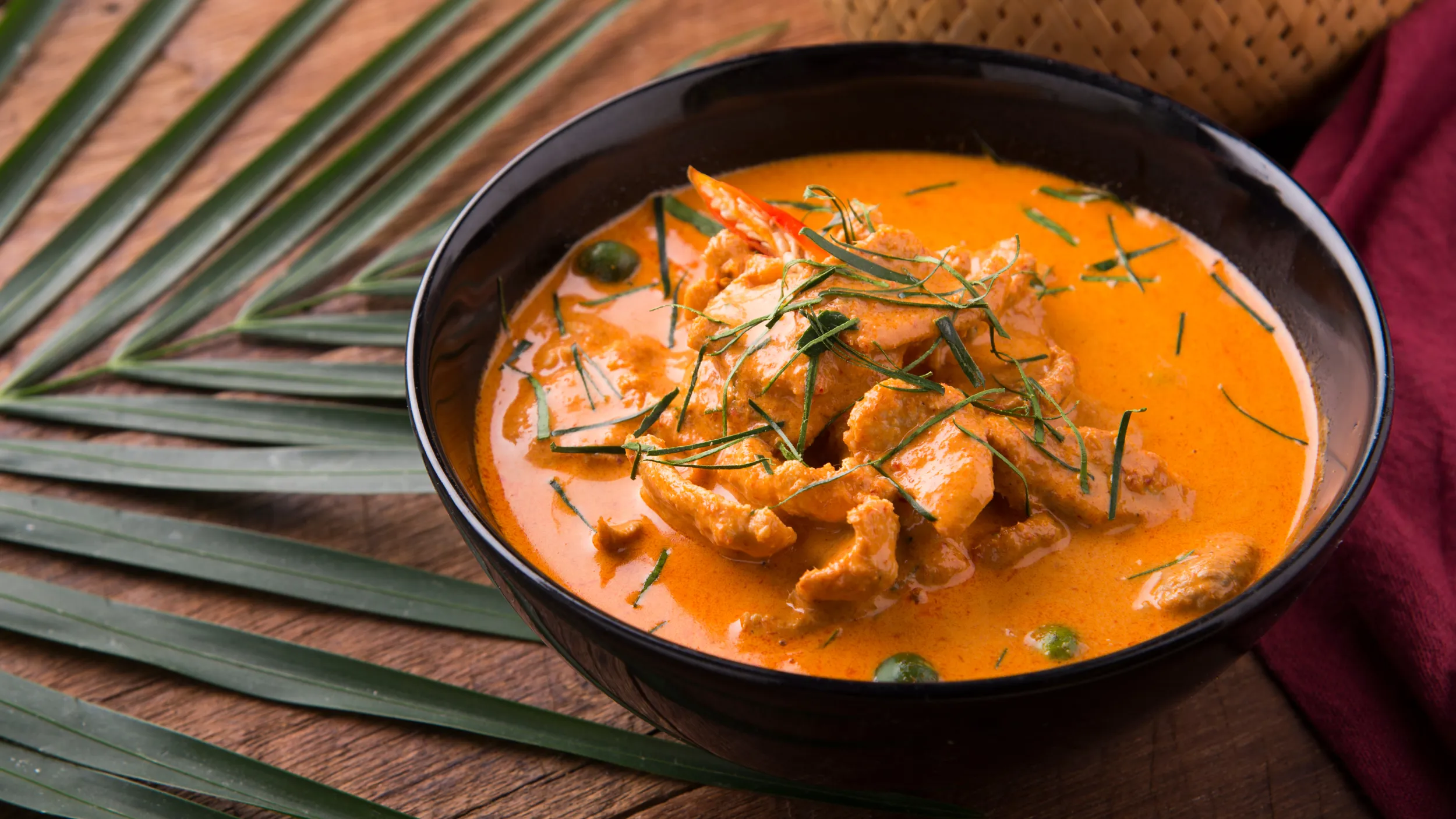 Ein rotes Thaicurry mit Fleisch und Kräutergarnitur.