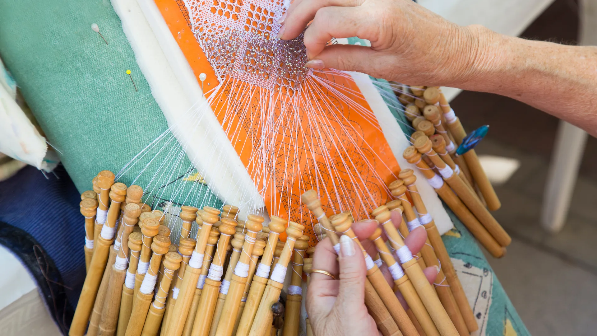 Nahaufnahme zweier Hände, die an einem Klöppel-Muster arbeiten.