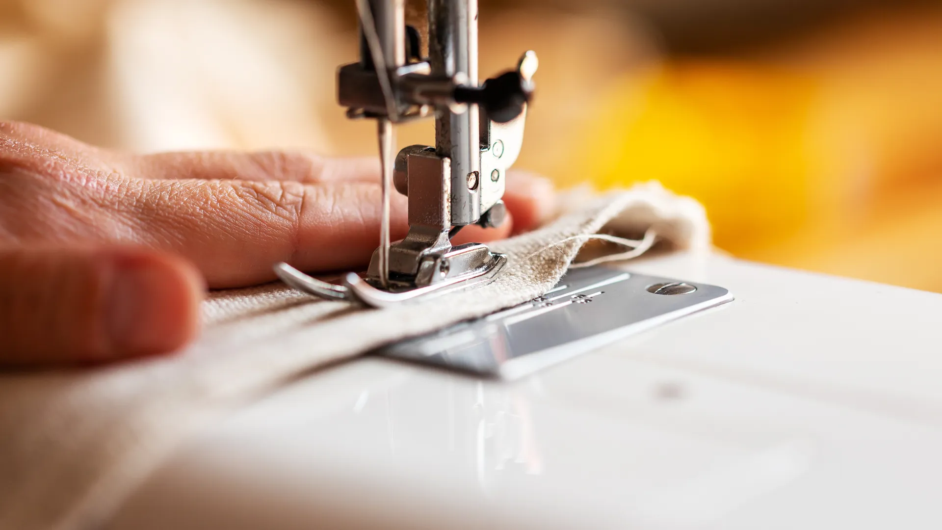 Nahaufnahme eines Nähmaschinenfuss, eine Hand führt den Stoff und näht.