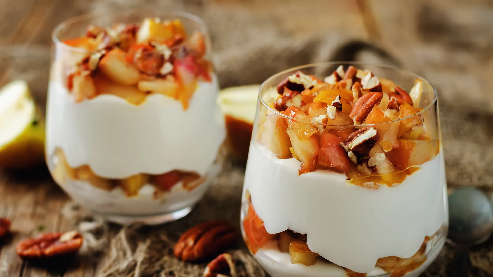 Zwei Desserts im Glas serviert mit Äpfeln und Nüssen.