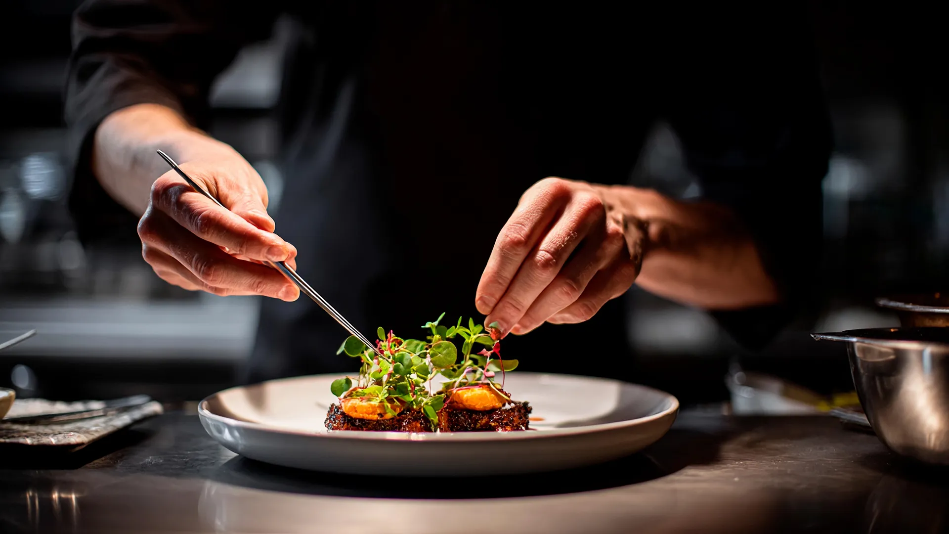 Ein Koch verfeinert ein kulinarisches Gericht mit Kräutern.