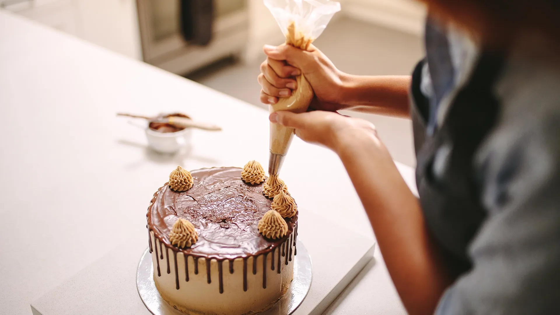 Eine Person dekoriert eine Schokoladentorte mit einer Spritztüte.
