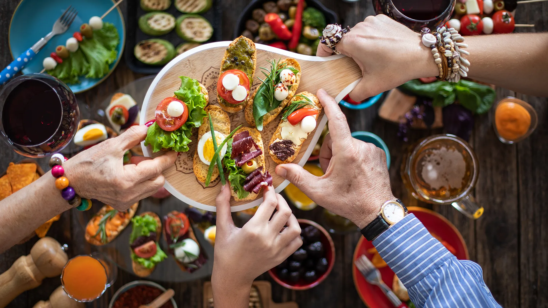Eine Person serviert auf einem Holztablett verschiedene Apéro-Häppchen.