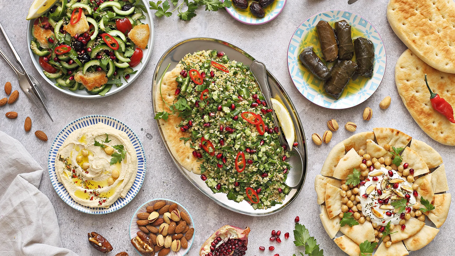 Orientalische Mezze-Platte: Taboulé, Hummus, gefüllte Weinblätter, Fladenbrot, Salat, Nüsse und Granatapfelkerne auf einem gedeckten Tisch.
