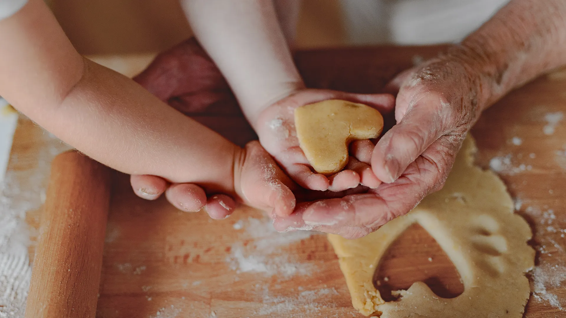 Ein älteres Paar Hände und Kinderhände stechen Kekse auch - nach Grossmutters Rezept.