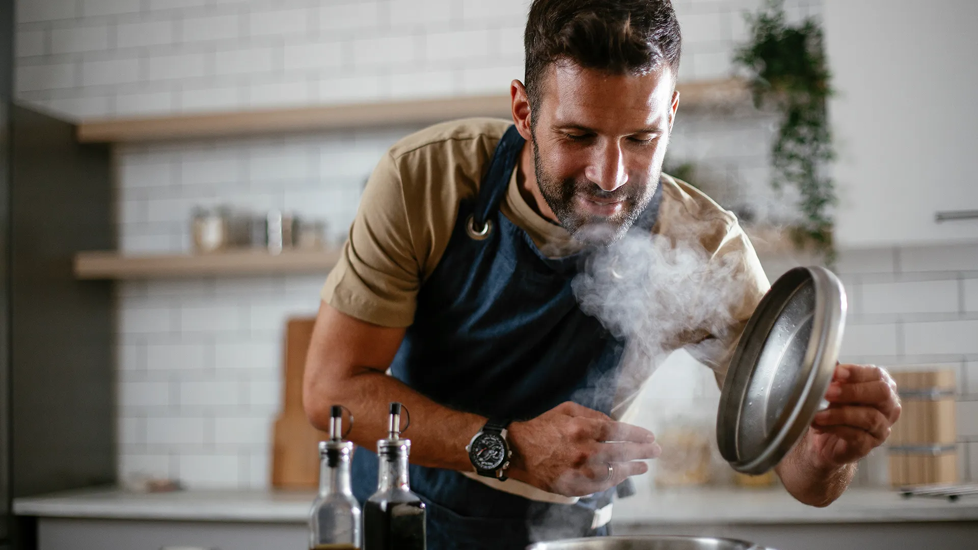 Ein Mann kocht ein Gericht und hebt den Pfannendeckel an.