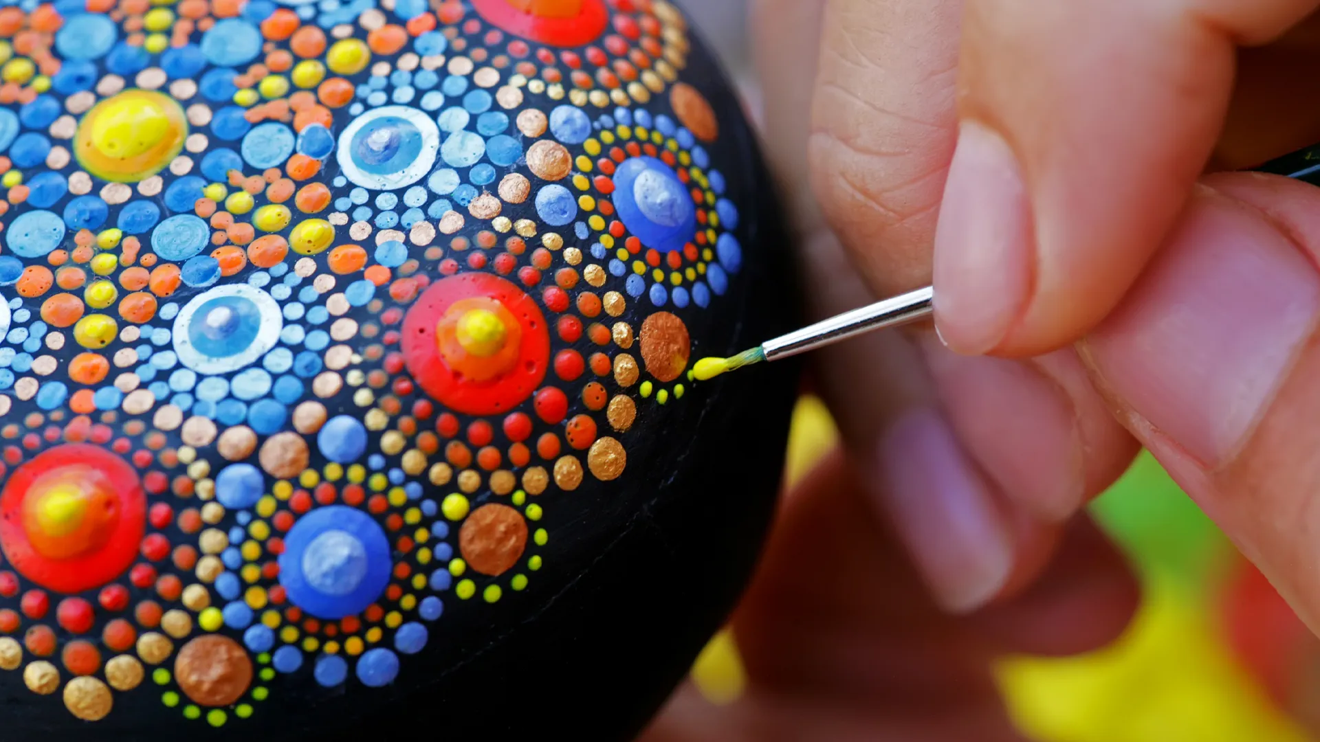 Hand bemalt einen Stein mit Dot-Painting-Technik, um ein punktbasiertes Muster zu gestalten.