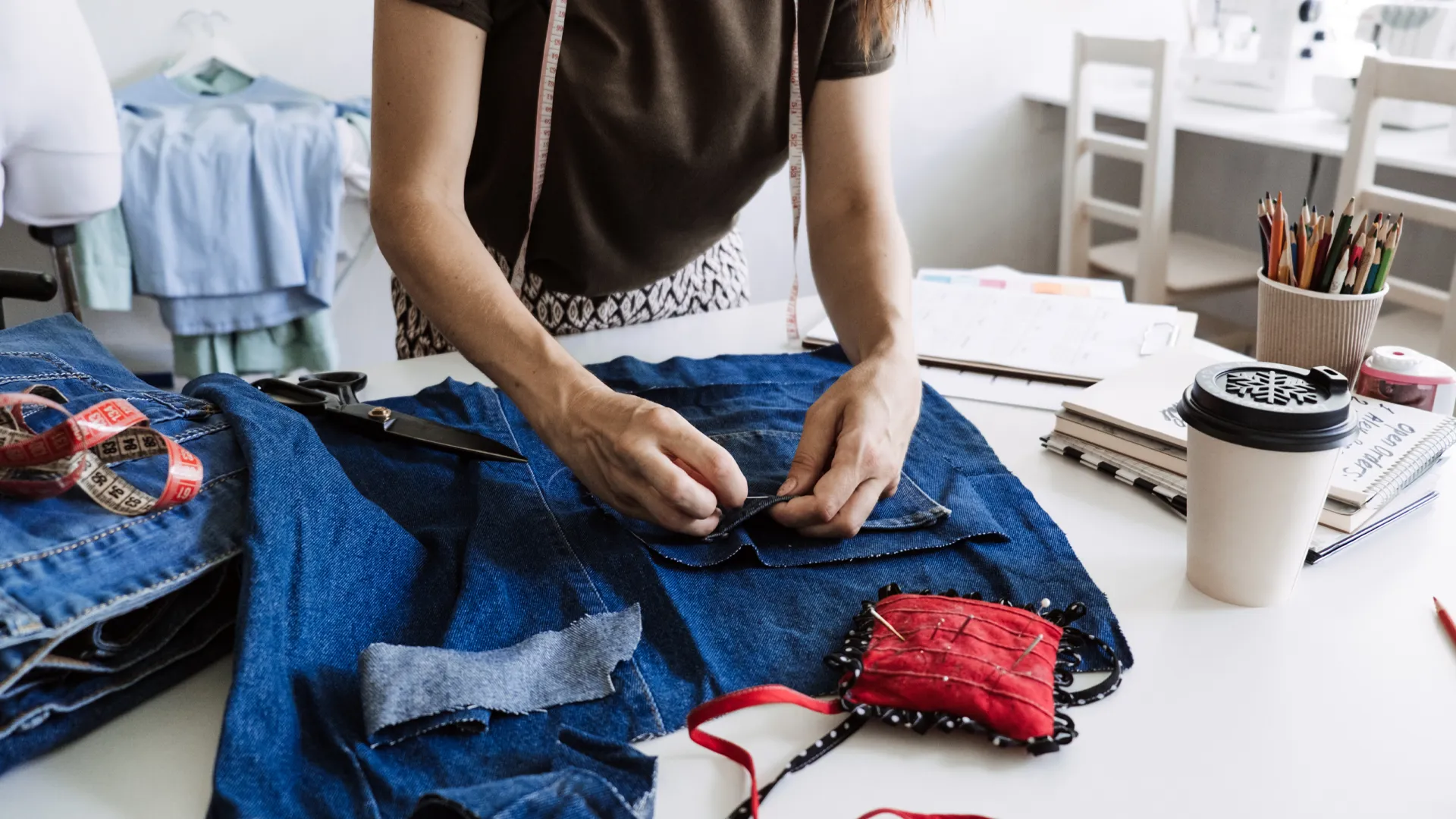 Eine Frau arbeitet an einem Upcycling-Projekt, indem sie alte Jeansstoffe zuschneidet und neu zusammennäht.
