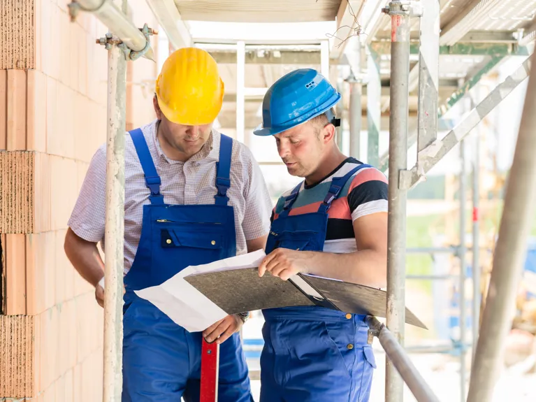 Zwei Mitarbeitende auf einer Baustelle besprechen gemeinsam Unterlagen