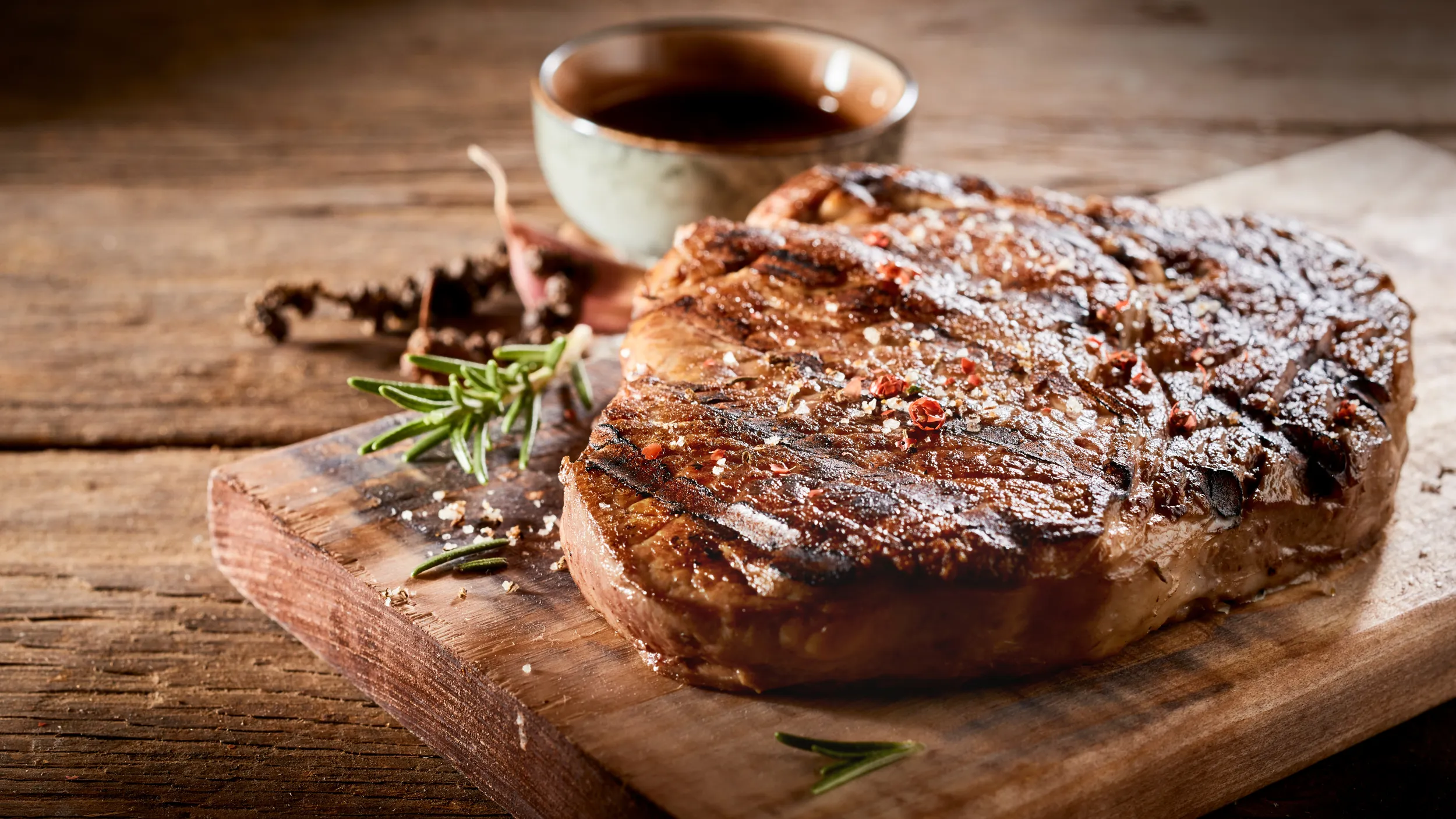 Ein Steak serviert mit Rosmarin und grobem Salz auf einer Holzplatte.