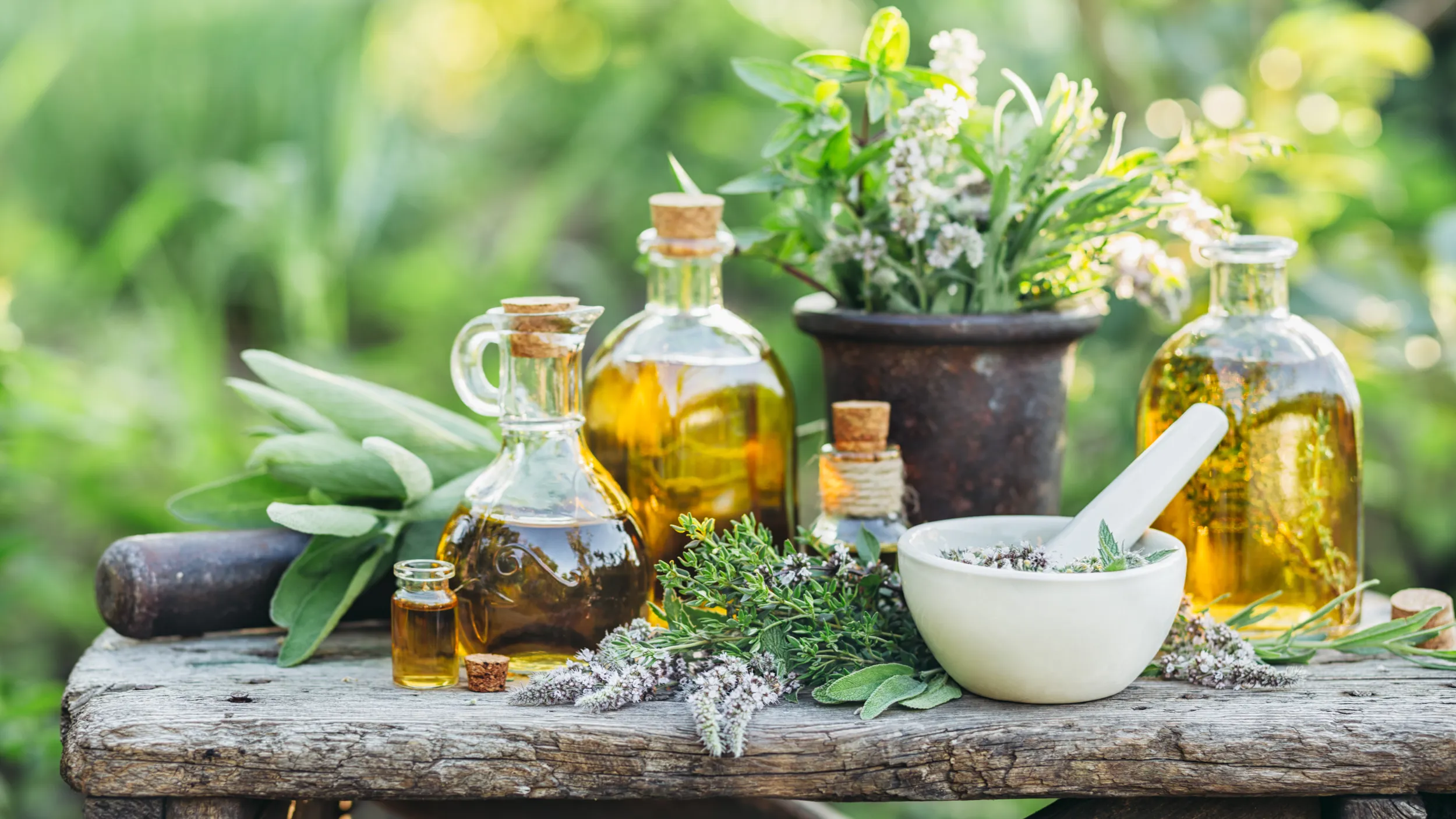 Verschiedene Kräuter und Öle stehen draussen auf einem Holztisch.