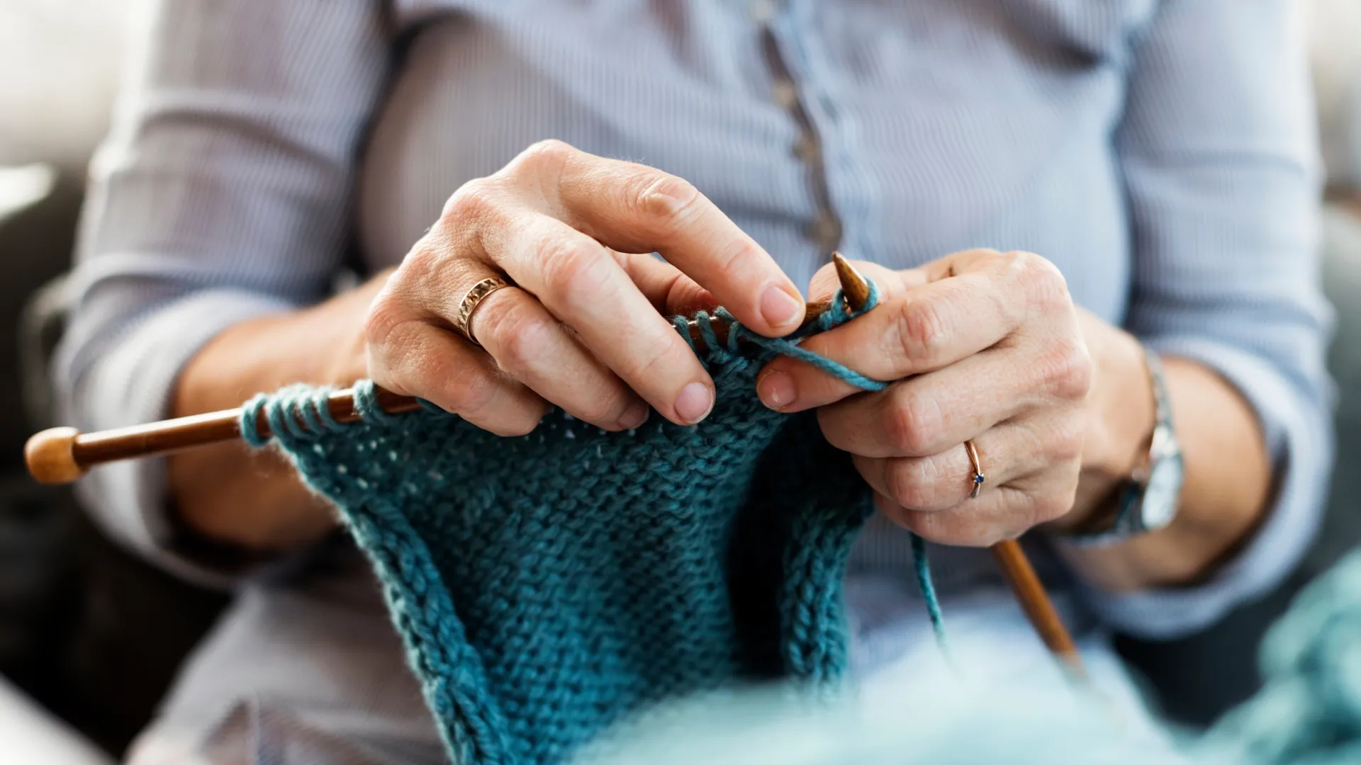 Nahaufnahme von Händen, die mit blauer Wolle stricken.