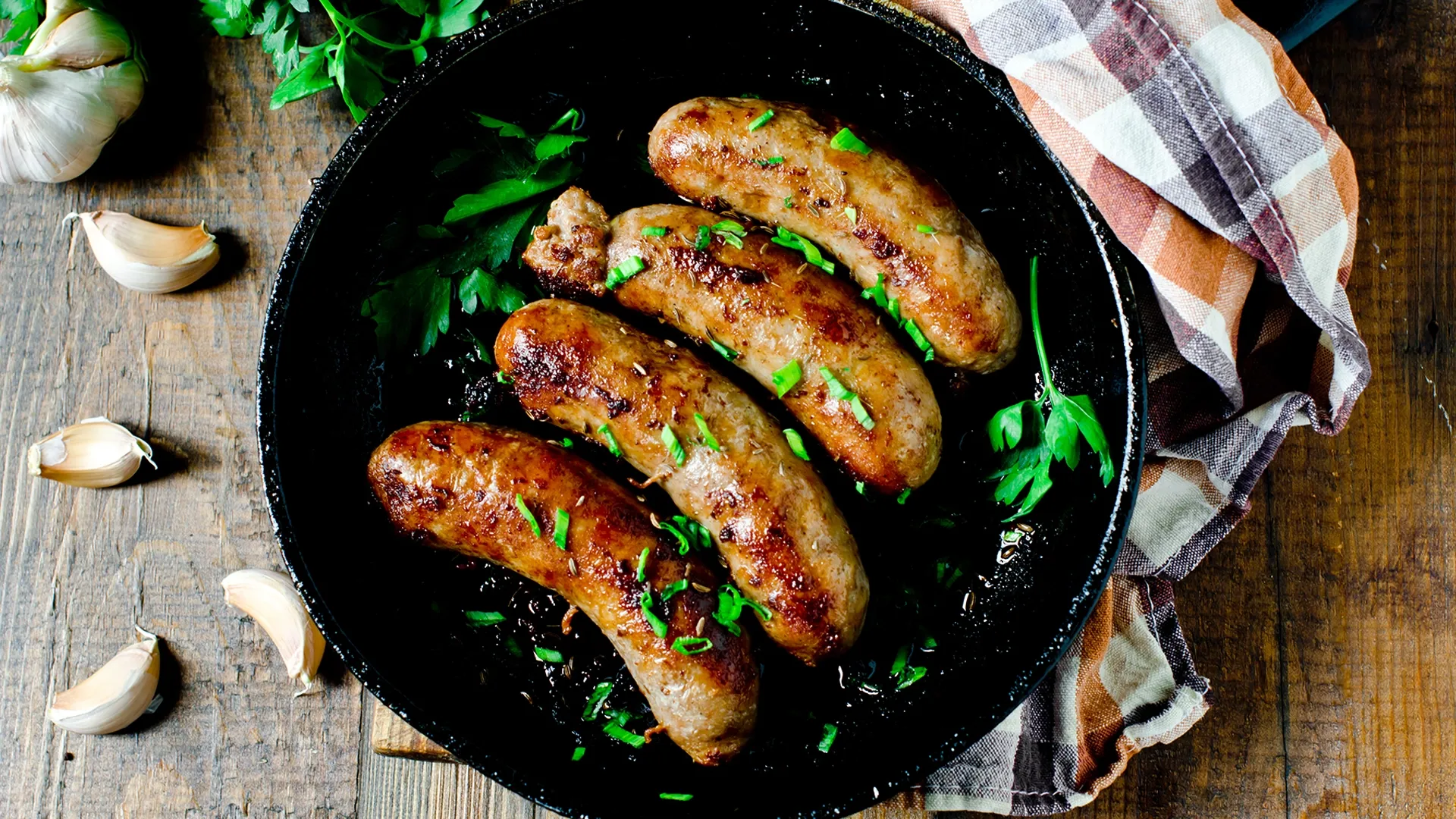 Vier Bratwürste liegen in einem schwarzen Teller mit Kräutern dekoriert.