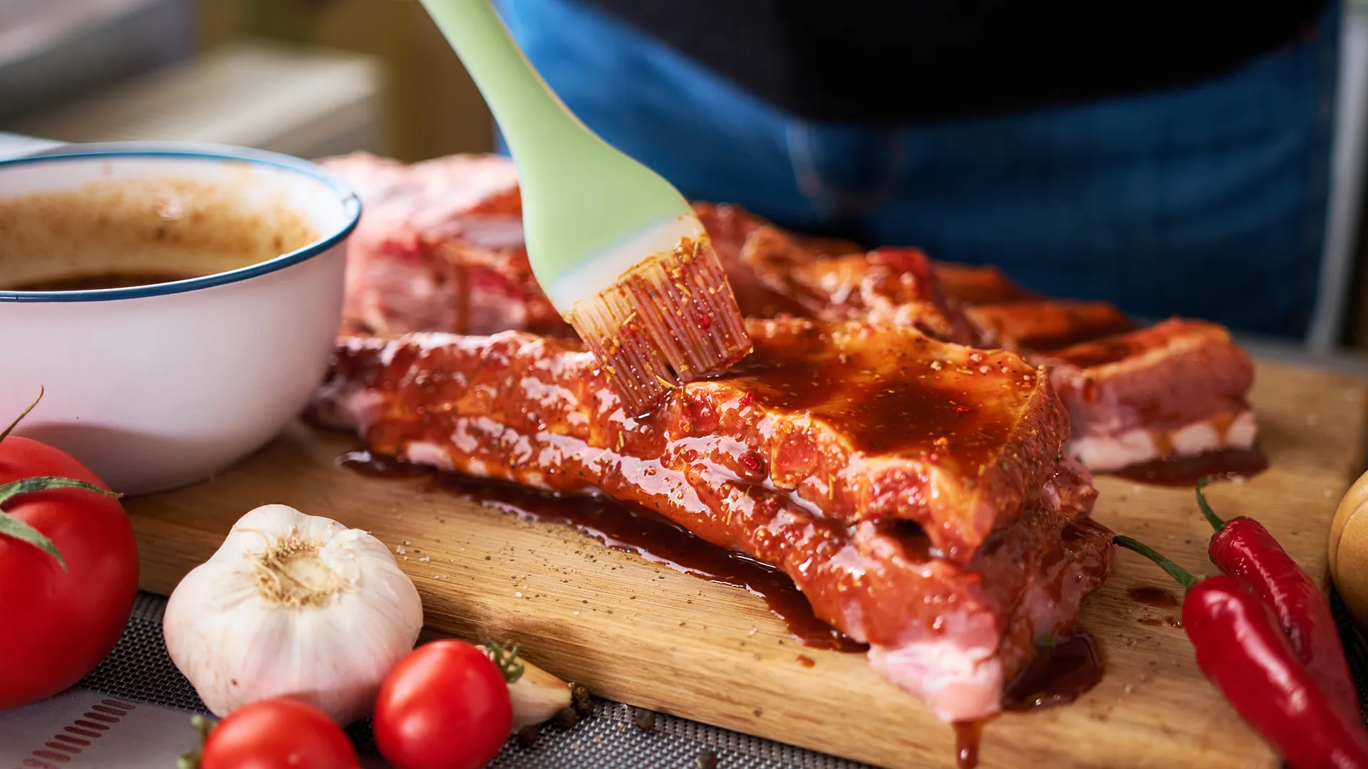 Eine Person bestreicht ein Stück Fleisch mit einer Grillmarinade.