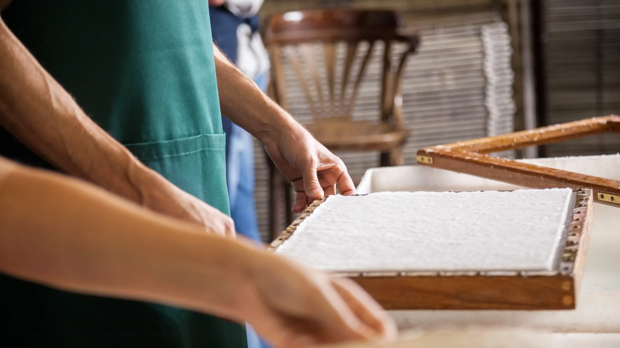 Zwei Personen schöpfen mit einem Holzrahmen Papier.