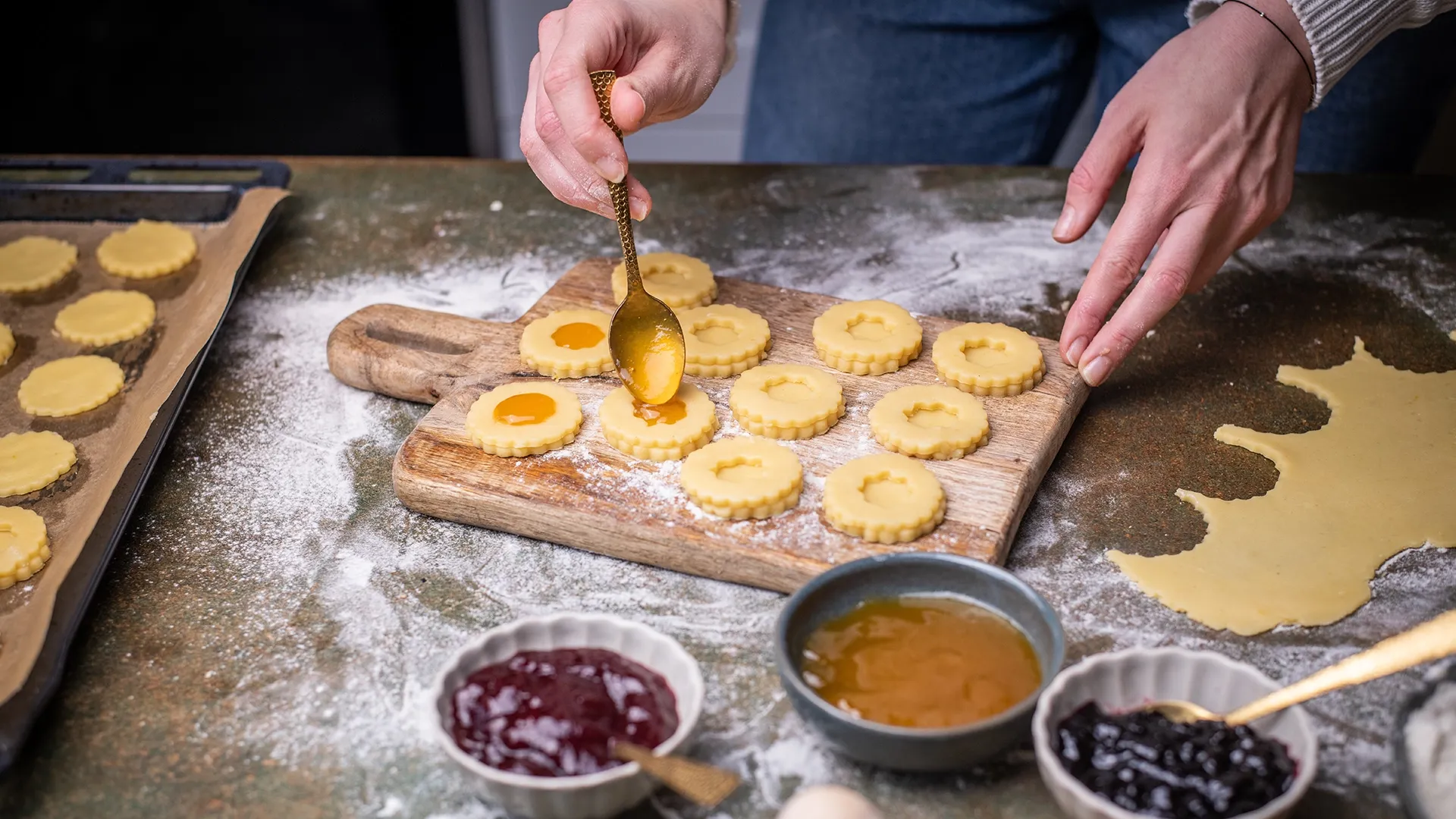 Eine Person füllt Weihnachtsguetzli mit Marmelade auf einem bemehlten Tisch.