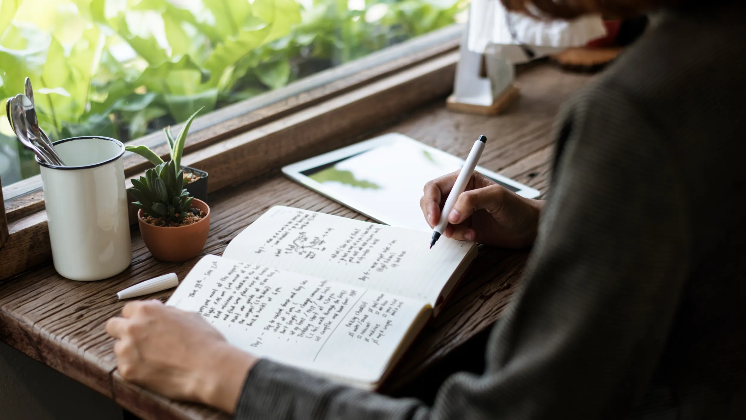 Eine Person sitzt am Fensterbrett, vertieft ins kreative Schreiben.
