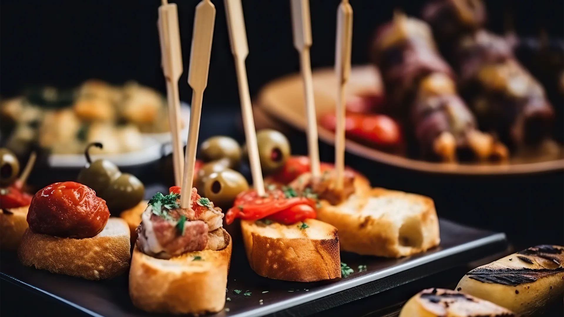 Verschiedene Tapas arrangiert auf einem schwarzen Teller.
