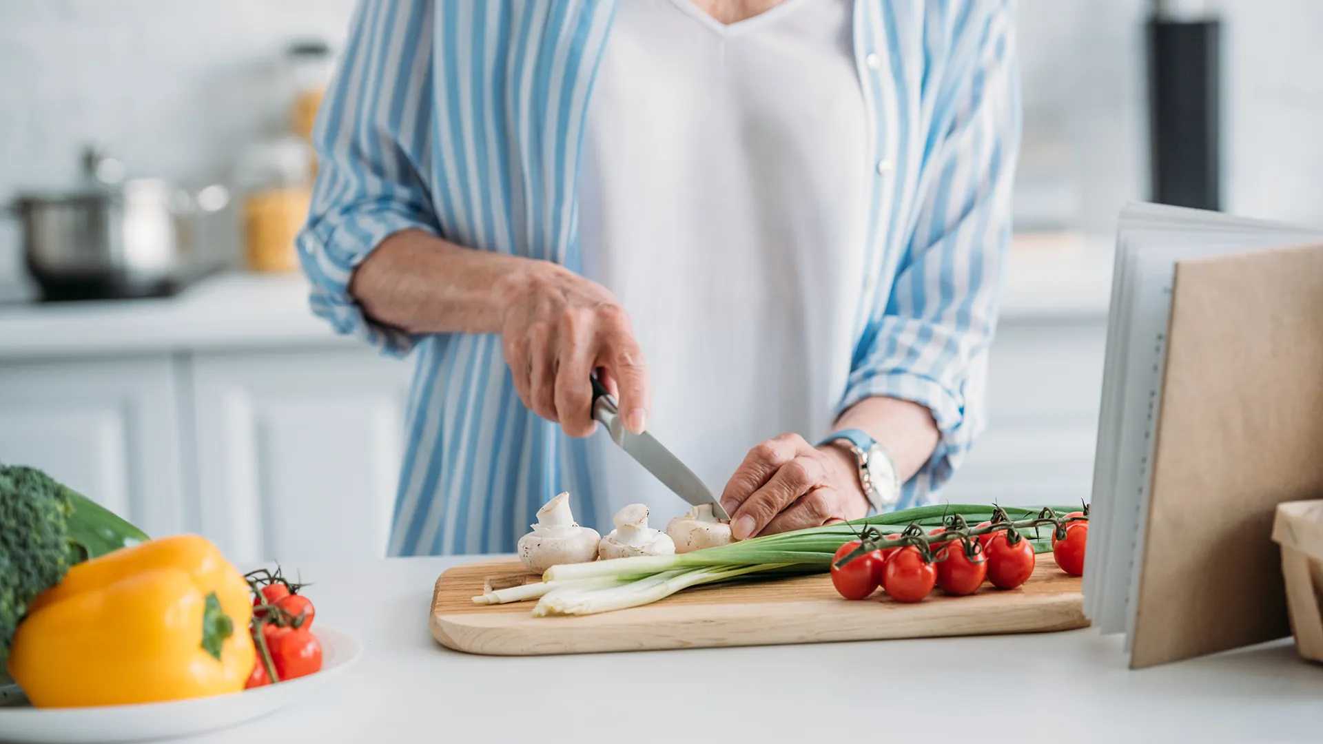 Eine ältere Person schneidet Gemüse auf einem Holzbrett.